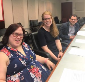 Two women and a man sit at a conference table and smile for the camera