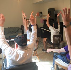 People sit in chairs with their arms up, practicing yoga. 