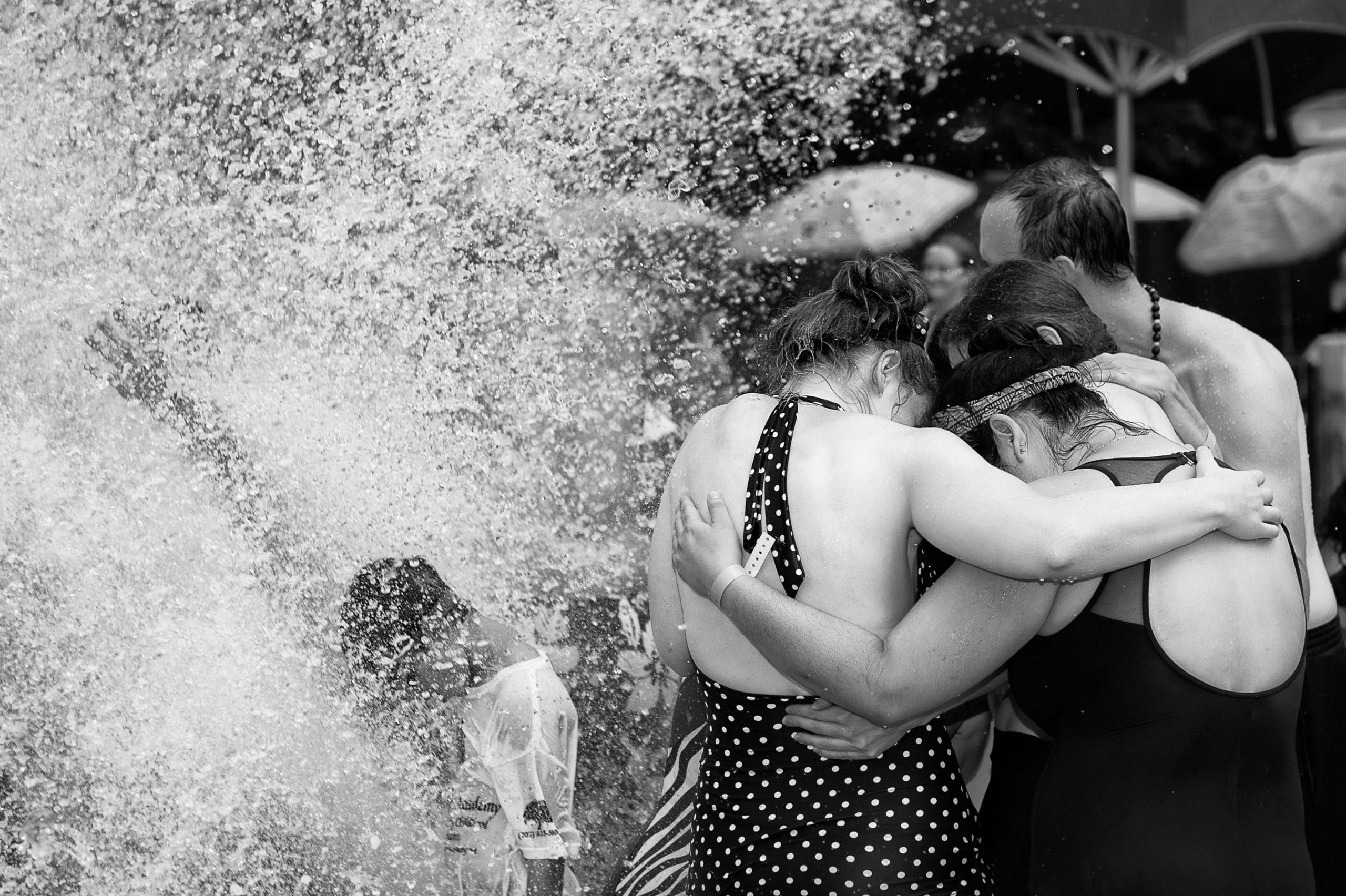 Women in bathing suits at a water park put their arms around each to shelter from a wave of water.