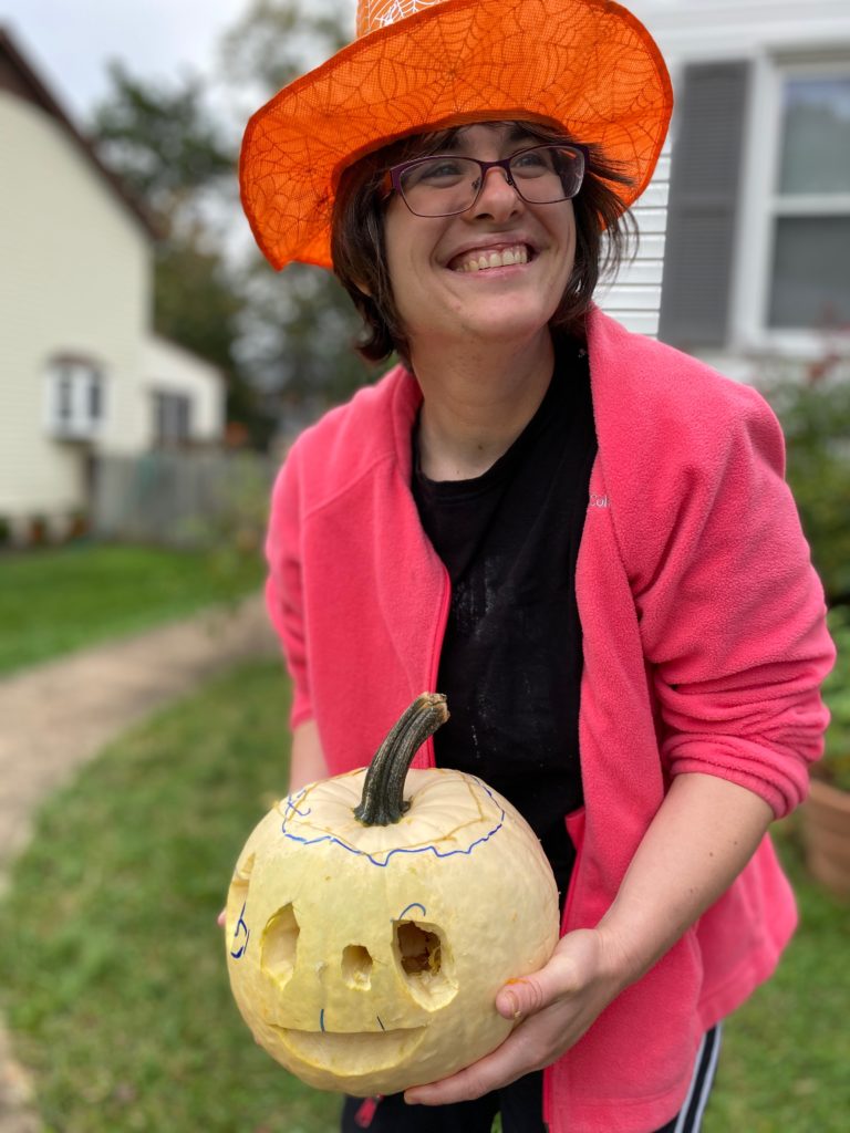 Woman in witch hat holding a pumpkin and smiling
