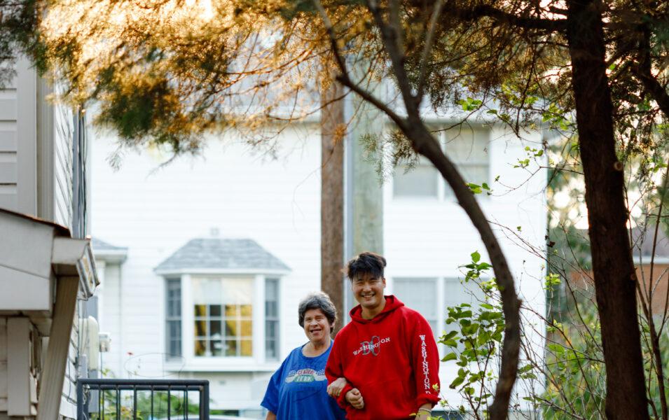 Fran and Joey are linked arms and smiling, walking toward Highland's backyard. The sunlight is breaking through the tree leaves above them.