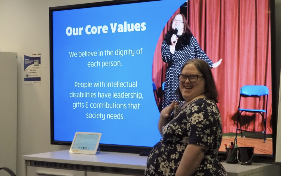 Laurie stands in front of a presentation screen. She is smiling and engaging.