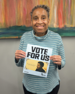 Eileen holding a paper that reads "vote for us" with the On Loneliness artwork.