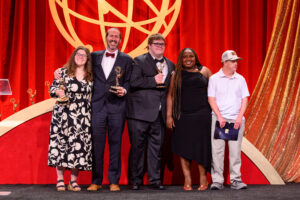 Five people standing on stage at the capital region Emmys for On Loneliness's win