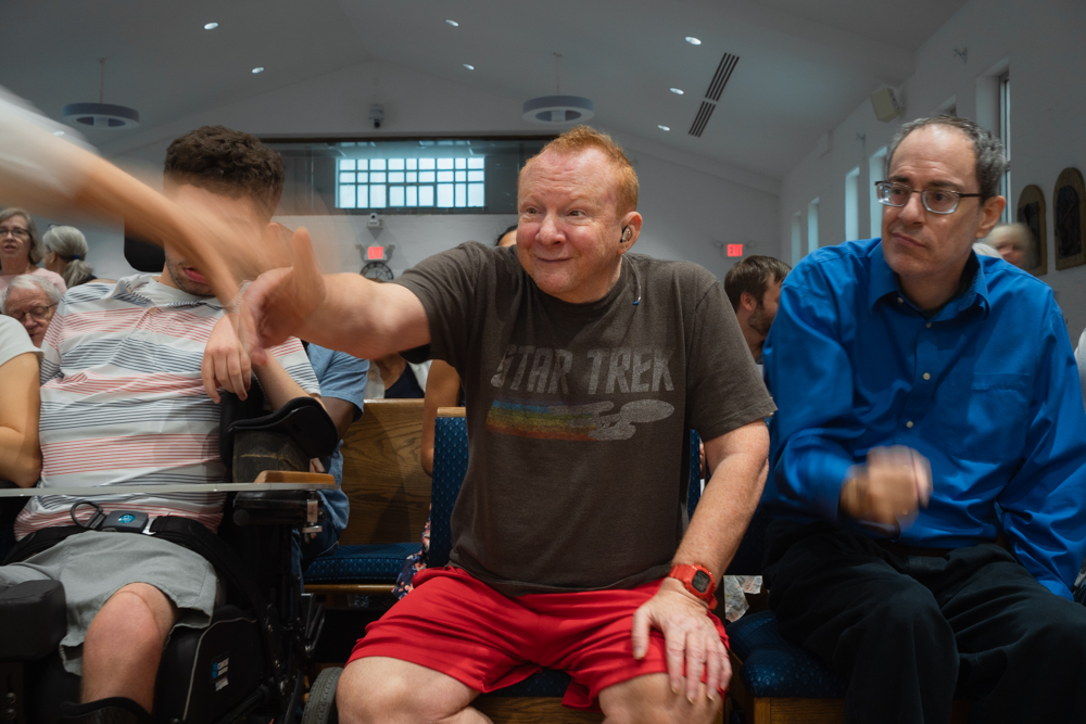 Eric is shaking a passerby's hand during mass at his church.