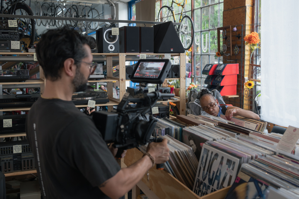 Josh films Eileen as she browses through records at a record store during the Sacred Stories Listening Tour.
