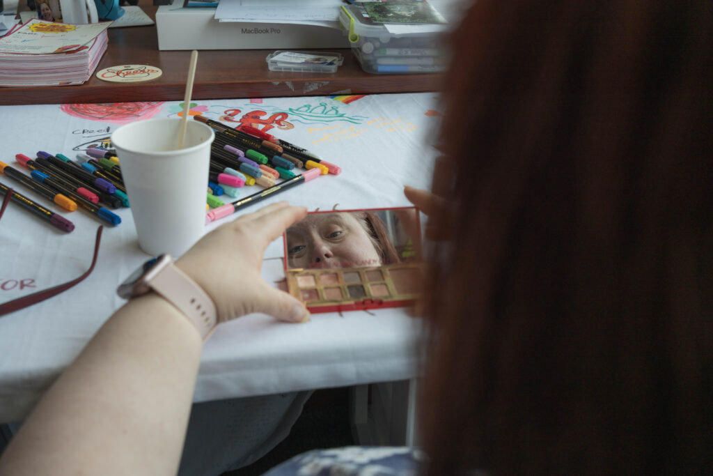 Laurie's hands hold a make-up mirror. We see her looking knowingly at her reflection. A paper coffee cup is nearby.